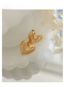 Macro shot of gold heart earrings with vintage lava texture on a white textured stand