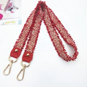 Detail of red and white woven shoulder strap with fringe and gold lobster clasp