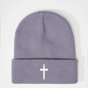 Detail of lavender knit beanie featuring a white embroidered cross on the cuff