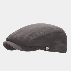 Detail of the silver brand emblem on a dark grey charcoal cotton flat ivy cap for men