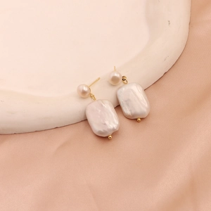 Detail of baroque pearl earrings with golden accents on elegant silk background