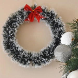 Close-up of a Christmas wreath featuring green and white needles with a red silk bow tie