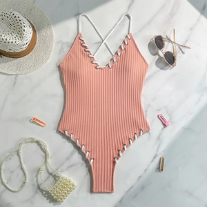 Detail of pink ribbed one-piece swimsuit with white lace-up ties on marble background
