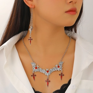 Detailed close-up of gothic silver bat and red gemstone cross necklace on a model