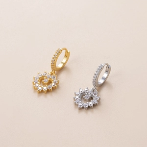 Detail von goldenen und silbernen Herzohrringen mit funkelnden Zirkonia auf rosa Grund