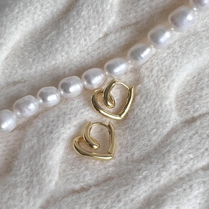 Minimalist gold heart hoop earrings on plush white background with decorative pearls
