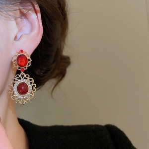 Detail of vintage gold earrings with red gemstones and floral hollow patterns on model