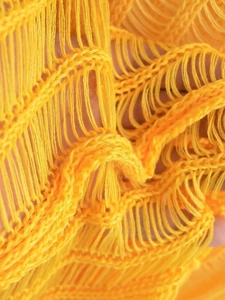 Detailaufnahme von gelbem Strickstoff mit durchbrochenem Hohlmuster und Fransenverzierung