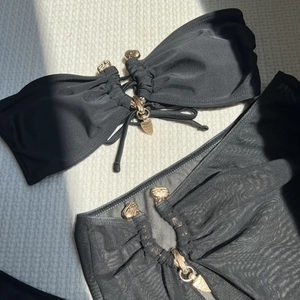 Détail du haut de bikini bandeau noir et paréo en résille avec boucles dorées