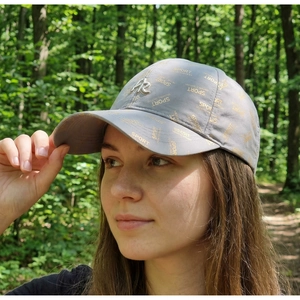 Close-up of grey quick-dry baseball cap with gold sport print and metal AR logo in nature