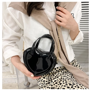 Detailed view of black heart-shaped glossy leather bag with gold chain strap on a model