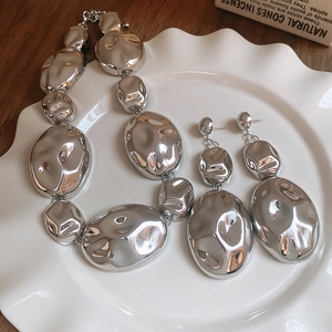 Detail of silver liquid metal necklace and earring set on white ceramic plate