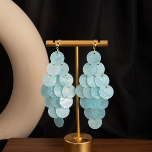 Detail of light blue layered disc drop earrings hanging on a gold jewelry stand
