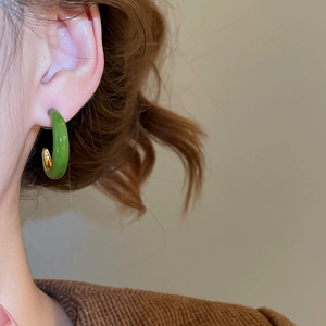 Close-up of forest green enamel C-shaped hoop earrings worn with golden metallic inner layer