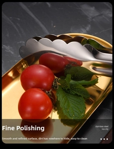Macro view of polished gold stainless steel food tongs on a mirror finish metal tray