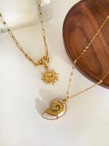 Detailed shot of gold sun pendant and spiral shell necklace on wooden decorative tray