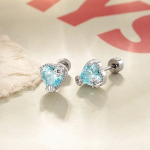 Silver heart earrings with light blue zircon and star accents on a beige fabric