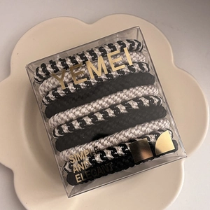 Detail of high-elasticity hair ties in a clear square box with gold brand text
