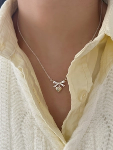 Close-up of a silver bow and heart pendant necklace worn on a neck for sweet style