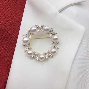 Detail view of a gold pearl wreath brooch with white pearls and zircons on a white blazer