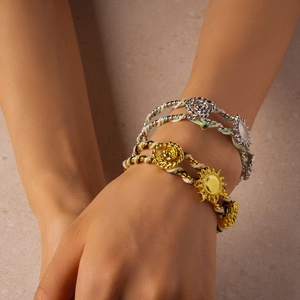 Close-up of woven rope bracelets featuring metallic sunflower and rose charms on wrist