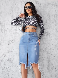Detail of high-waist blue denim skirt with distressed ripped hem and front slit design