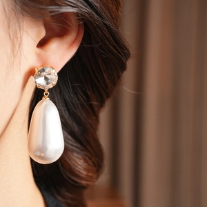 Détail d'une boucle d'oreille en perle goutte avec clou en cristal doré sur un modèle