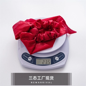 Detailed view of a red pleated fabric bow scrunchie on a scale weighing 23.5 grams