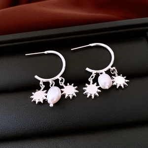 Macro detail of silver C-hoop earrings featuring baroque pearls and sun charms