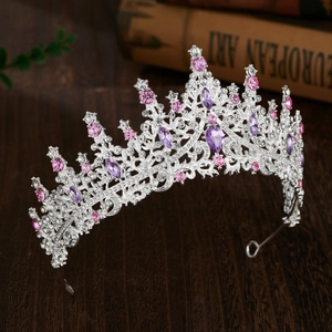 Close-up of silver bridal crown with pink and purple crystals on dark wood surface