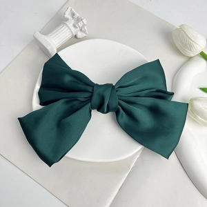 Detail of elegant dark green satin bow hair clip on a minimalist porcelain display tray