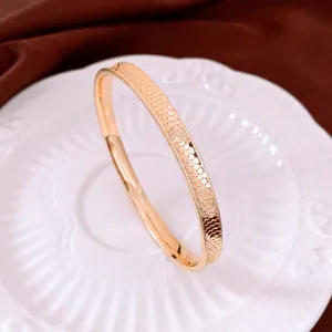 Elegant gold metal bangle with honeycomb texture and beaded edge on a white ceramic plate