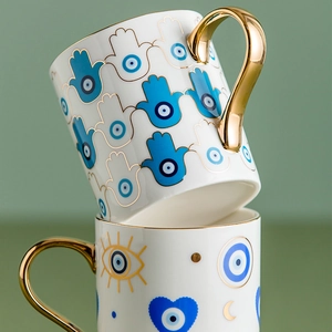 Close-up of ceramic mugs with gold handles and Hamsa hand plus evil eye patterns