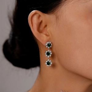 Detail of elegant three-tier floral drop earrings featuring green emerald stones and diamonds