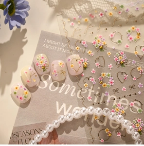 Detail of floral nail stickers with gold outlines on a soft white manicure finish