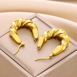 Detail of 18K gold-plated twisted hoop earrings on a beige textured jewelry box