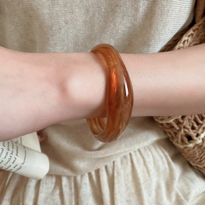 Detail shot of amber acrylic wide bangle featuring translucent resin finish and smooth texture