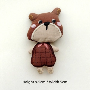Detail of a brown fabric bear doll with plaid apron, measuring 9.5cm high and 5cm wide