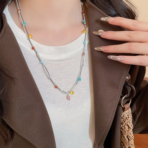 Detail of bohemian layered stone necklace with pink droplet pendant on white shirt