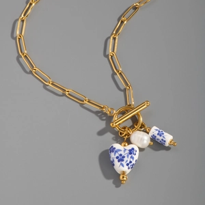 Detail of blue floral porcelain heart and pearl pendant on golden T-bar chain necklace
