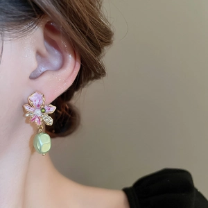 Detail of flower earring with pink-purple enamel petals and green irregular pearl drop