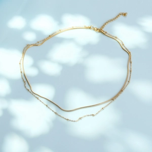 Double-layered gold snake chain necklace with small beads and extension on blue background