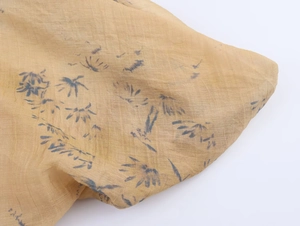 Close-up of thin v-neck top fabric with blue floral print on yellow-brown texture