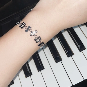 Detailed close-up of a silver music note bracelet worn over a piano keyboard background