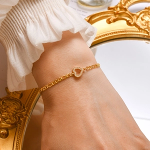 Detail of 18K gold heart bracelet with zircon stones worn on wrist against a vintage mirror