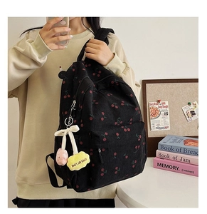 Close-up of black corduroy backpack with red cherry prints and plush charm pendant