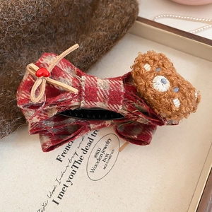 Detail of a plush bear and red plaid bow hair clip on a cozy wooden tray setting