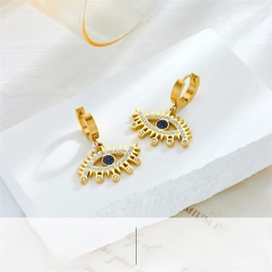 Detail of gold evil eye earrings with blue crystals and pavé stones on a stone plate
