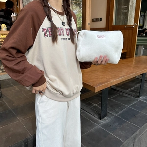 Soft white faux shearling cosmetic bag with red label shown in an outdoor lifestyle setting