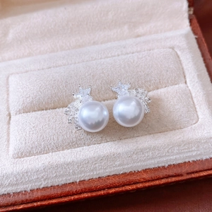 Macro view of silver earrings with white pearl and star zircon inlay on beige velvet